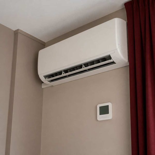 White ductless mini split air handler mounted in the corner of a taupe bedroom wall with a digital wall thermostat below